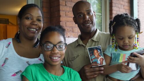 mother, father who is holding photo of daughter, and two daughters