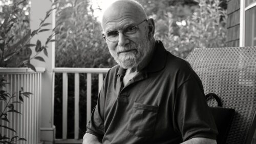 black and white photo of man sitting on porch