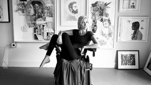 Kelsey posing on a chair with a wall of pictures in frames behind her