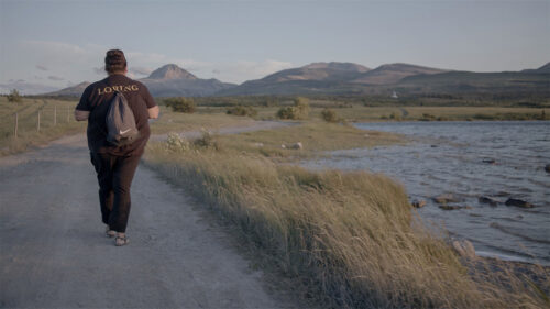 person walking on path next to water with their back to the viewer