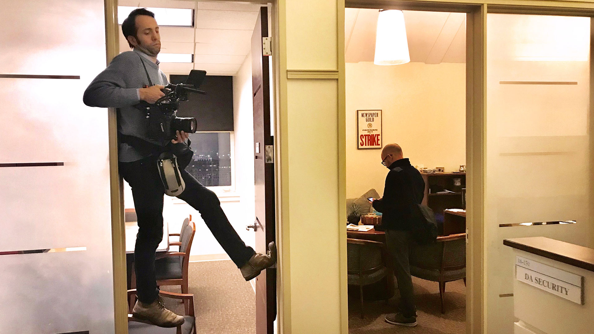 Yoni Brook with camera balanced precariously in doorway in D.A. office