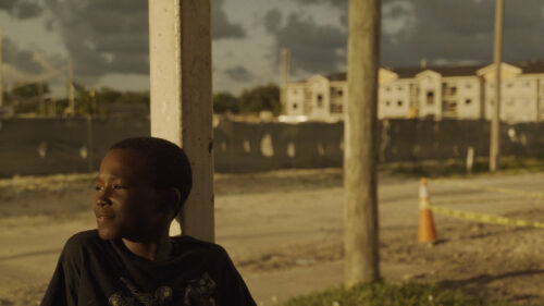 Young boy looking into distance with broken down road behind him
