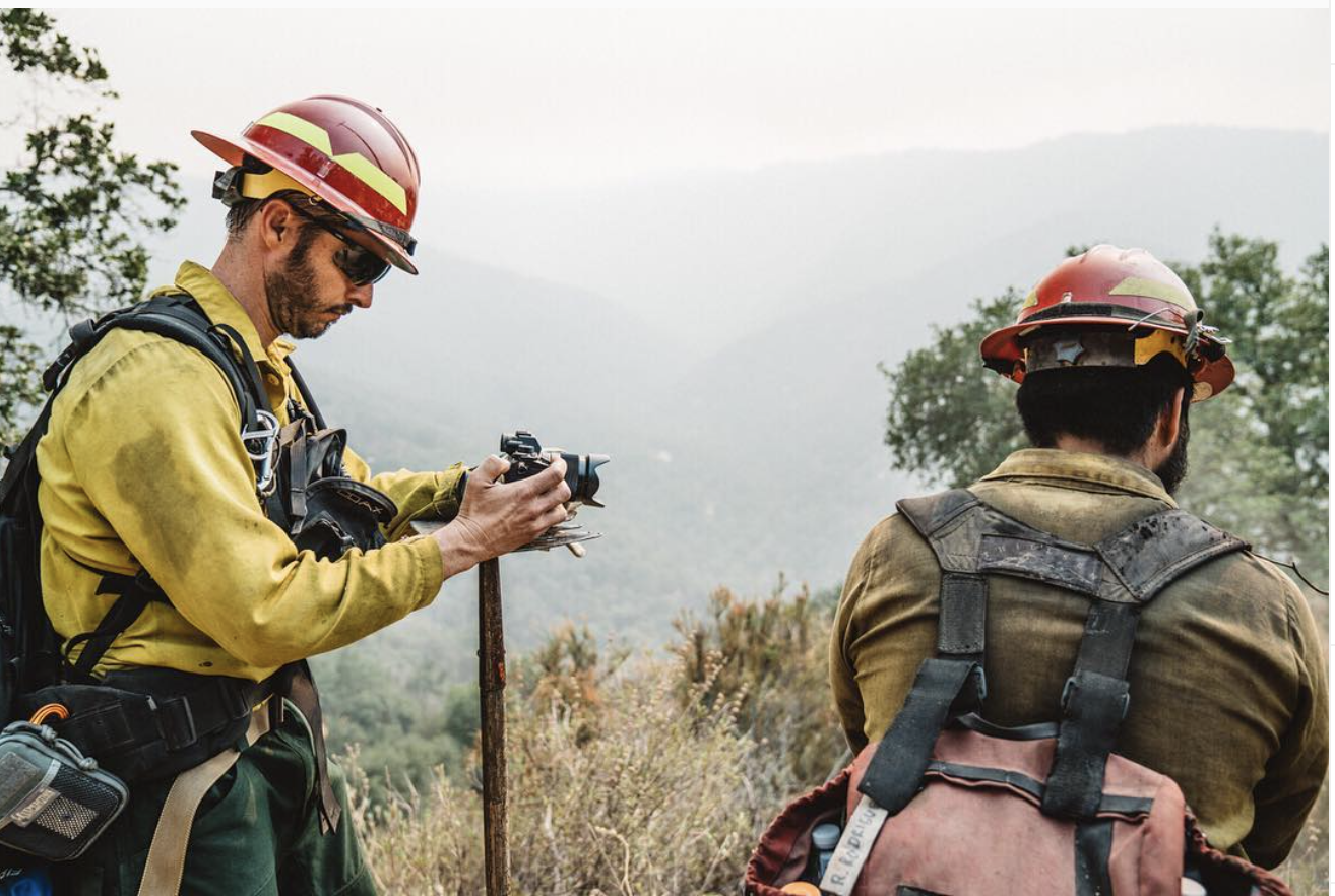 Alex Jablonski filming Wildland while wearing firefighter gear alongside fire crew, and looking through camera