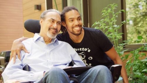 two men smiling one in a wheelchair 