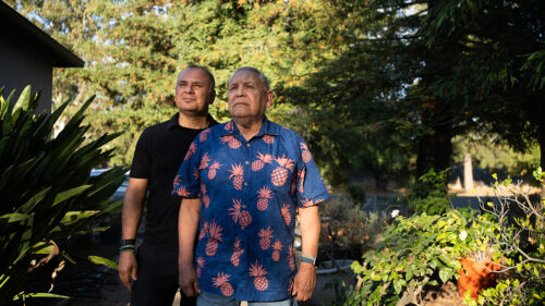 two men who look like father son in a garden looking beyond the camera