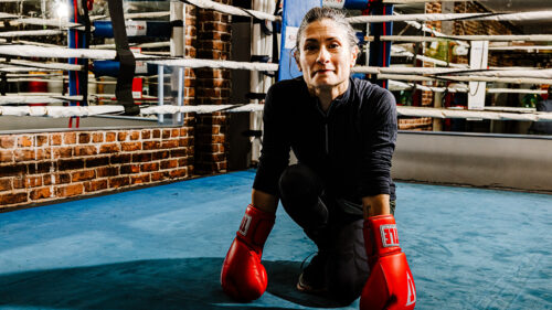 Woman with boxing gloves on crouched looking at the camera