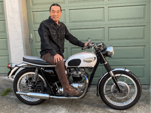 middle age asian man with hair pulled back into a ponytail sitting on a motorcycle