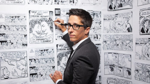 Comic Alison Bechdel in front of wall of comics