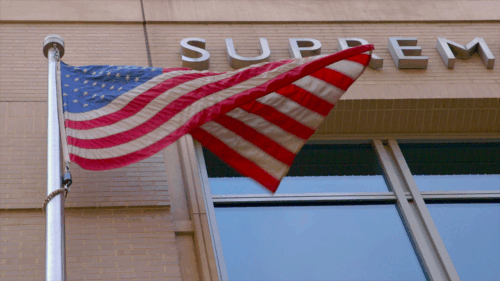The American flag flies in front of a brick courthouse.