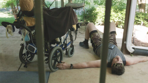 Man lying on the ground next to a wheel chair