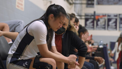 Young asian woman in basketball uniform crying with coach in mask talking to her
