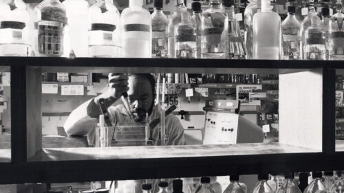 Man working in medical lab wearing a lab coat with light skintone and using a pipette
