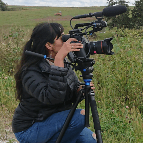 Woman with dark hair looking through large film camera