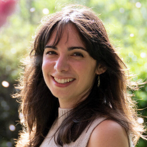 headshot of woman in garden smiling with long brown hair