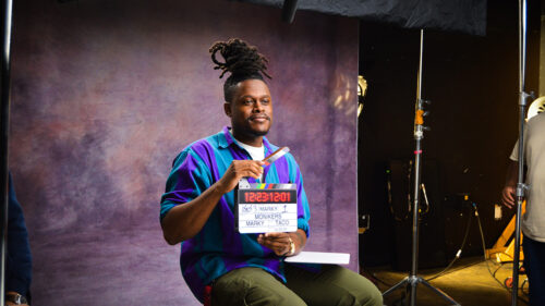 Man holding film clapper looking away from camera in front of photo background