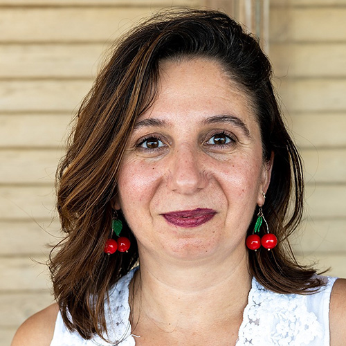 Woman with brown hair and cherry earrings looking into the camera