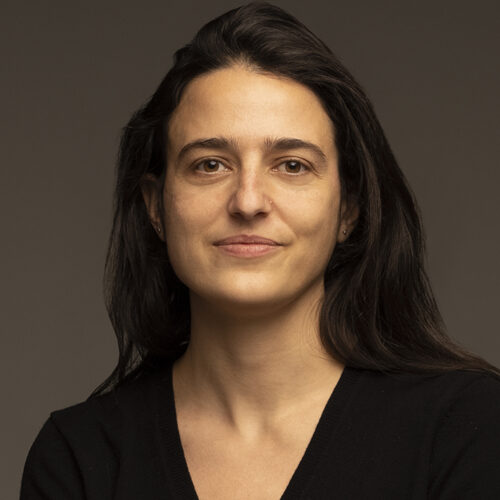 White woman with dark hair in a white t-shirt, slight grin on her face