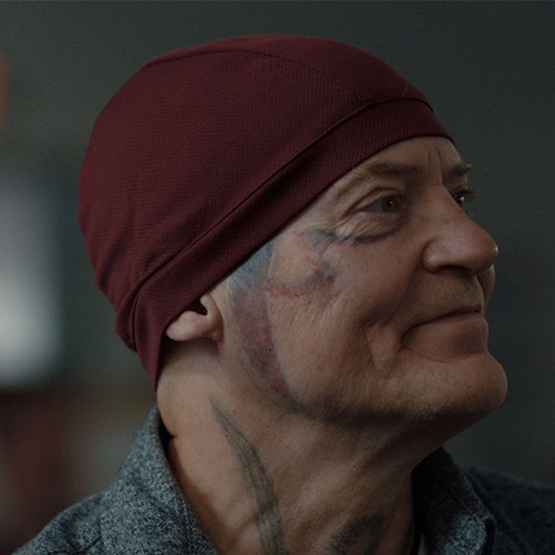 Headshot of man wearing a beanie with large tattoos on neck and face