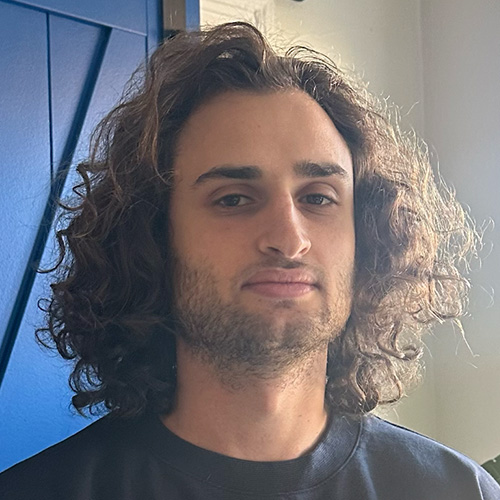 Headshot of man with curley brown hair down to shoulders light skin tone