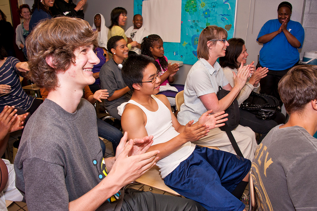 A room of high school age looking people clapping looking in the same direction off camera