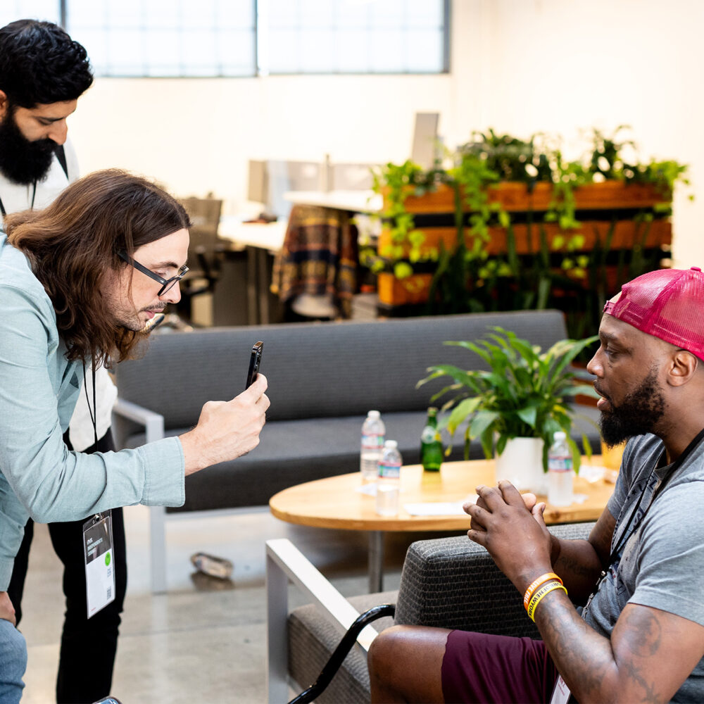 Man taking video on cell phone of man sitting in a chair. Man on camera appears to be talking