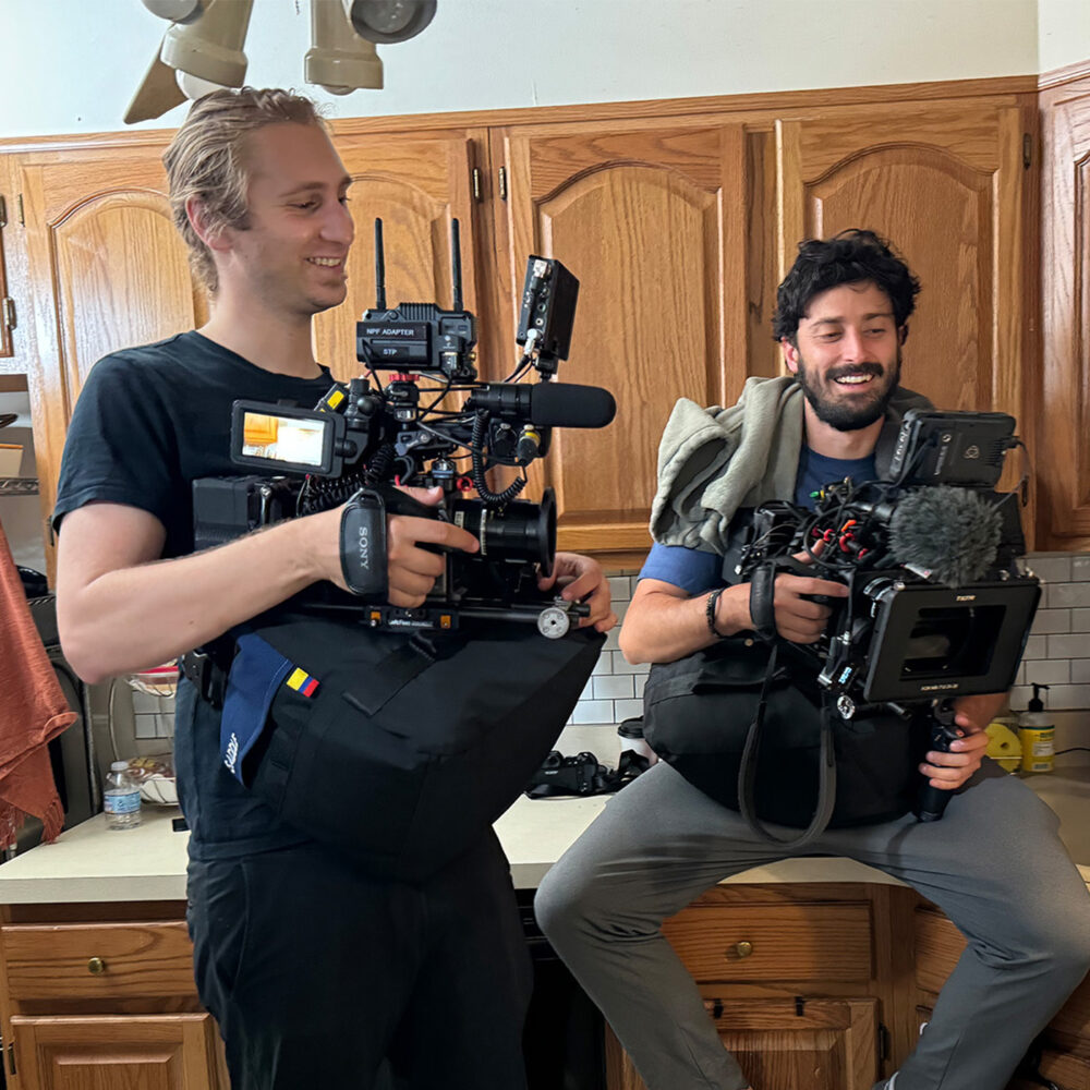 two men in a kitchen smiling holding camera equipment