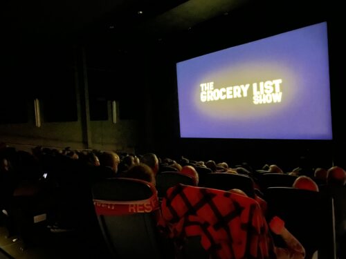 A movie theater audience faces a screen displaying the title 