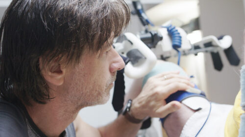 A man adjusts a blue strap on a patient’s knee during a rehabilitation session.